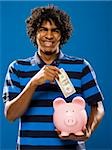 young man putting money in a piggy bank.