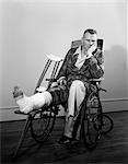 ANNÉES 1950 JAMBE DE L'HOMME EN FAUTEUIL ROULANT EN FONTE AVEC DES BÉQUILLES À CÔTÉ EN REGARDANT LA CAMÉRA