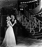 1940s ROMANTIC COUPLE MAN AND WOMAN FORMALLY DRESSED DANCING NEAR ART DECO STAIRCASE