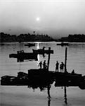 1970s PEOPLE FISHING OFF OF DOCK WITH SMALL BOATS IN BACKGROUND AT DUSK