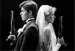 1980s BRIDE AND GROOM BACK TO BACK HOLDING DUELING PISTOLS