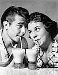 1950s ROMANTIC TEENAGE COUPLE BOY AND GIRL HEAD TO HEAD DRINKING MILKSHAKES