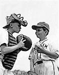 1950s TWO BOYS WEARING LITTLE LEAGUE BASEBALL UNIFORMS THE CATCHER IS GIVING ADVICE TO PITCHER