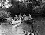 ANNÉES 1930 5 GENS HOMMES FEMMES DANS 2 PIROGUES QUI DESCEND UNE COURS D'EAU L'ÉTÉ DE RAMES