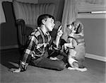 1950s BOY IN PLAID SHIRT SHAKING FINGER AT DOG SITTING UP ON REAR LEGS