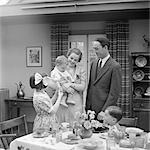 1930s FAMILY OF 5 IN DINING ROOM MOTHER STANDING HOLDING BABY