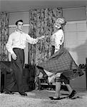 1950s TEEN COUPLE DOING THE JITTERBUG IN LIVING-ROOM