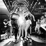 1970s COUPLE DISCO DANCING ON ROLLER SKATES WEARING TRENDY CLOTHES UNDER A MIRRORED BALL