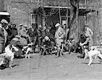 1920s 1930s HUNTING DOGS WITH TRAINERS ASSEMBLED FOR FIELD TRIALS IN FRONT OF BRICK BUILDING