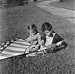 ANNÉES 1940 FILLE ET GARÇON ASSIS DANS L'HERBE PELOUSE HOLDING KITE STYLE DRAPEAU AMÉRICAIN