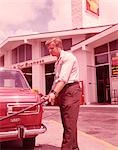 1960s RED CAR AT PUMPS WITH GAS STATION ATTENDANT