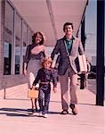 1960s FAMILY OF 3 WALKING DOWN STREET CARRYING PACKAGES