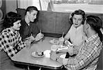 ANNÉES 1950 DEUX JEUNES COUPLES AU STAND EN SALLE À MANGER PORTANT DES CHEMISES PLAID ET DE COULEUR UNIE, BOIRE DES BOISSONS GAZEUSES PARLER ENSEMBLE