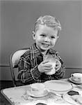 1950s SMILING BOY IN PLAID SHIRT DRINKING MILK AT CARD TABLE HAPPY NUTRITION SNACK COOKIES