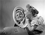 1950s SMILING WOMAN WEARING AN OFF THE SHOULDER RUFFLED BLOUSE LOOKING INTO A OVAL MIRROR AT HER REFLECTION