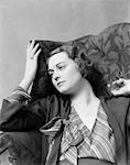 1930s WOMAN SITTING IN HIGH BACK CHAIR WITH A THOUGHTFUL OR MELANCHOLY FACIAL EXPRESSION