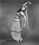 1960s WOMAN IN BELLY-DANCER COSTUME STRETCHING BACK WITH ARMS OUT