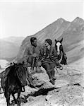 1920s 1930s COUPLE SITTING ON ROCKS HOLDING REINS OF TRAIL HORSES