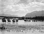 1930s GROUP FOUR MEN RIDING HORSES THROUGH SHALLOW END OF RIVER TRAILING LINE OF HORSES BEHIND HORSE RIVER ALTA