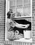 1930s WOMAN SITTING BACKWARDS ON WINDOW LEDGE WASHING WINDOW PANES