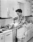 1950s WOMAN HOUSEWIFE IN KITCHEN APRON MIXING BAKING INGREDIENTS IN BOWL