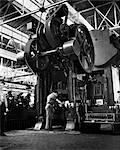 1940s BACK VIEW OF MAN WORKING AT GIANT STEEL PRESS