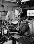 1960s CLOSE-UP OF ELDERLY MAN IN CAP & GLASSES WITH PENCIL BEHIND EAR WORKING ON LATHE IN INDUSTRIAL FACTORY SETTING