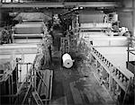 1970s PARTIAL OVERHEAD LOOKING DOWN AISLE OF PAPER FACTORY WITH LARGE ROLLERS TO EITHER SIDE