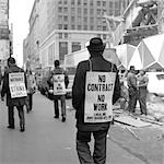 1970s REAR VIEW OF MAN WALKING DOWN SIDEWALK WEARING NO CONTRACT NO WORK SIGN WITH OTHER PICKETERS IN BACKGROUND