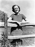1940s PORTRAIT SMILING YOUNG GIRL WOMAN LEANING ON WOODEN FENCE