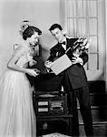 1950s TEEN COUPLE BOY AND GIRL IN PROM FORMAL WEAR PLAYING PHONOGRAPH RECORDS IN HOME LIVING ROOM