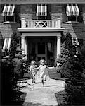 1930s 2 GIRLS IN SUMMER DRESSES RUNNING TO CAMERA ON FLAGSTONE SIDEWALK IN FRONT OF HOUSE