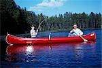 1960s GRANDFATHER & BOY RED CANOE ON LAKE FISHING GRANDSON REELING IN FISH CATCH FAMILY FAMILIES GENERATIONS