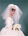 1960s SMILING HAPPY BRIDE PORTRAIT SEATED SITTING WHITE WEDDING GOWN BRIDAL BOUQUET FLOWERS SHORT NET VEIL