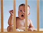 1960s BABY IN CRIB LOOKING THROUGH BARS ARM RAISED OPEN MOUTH
