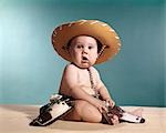 1960s BABY WEARING COWBOY COSTUME WITH FUNNY FACIAL EXPRESSION