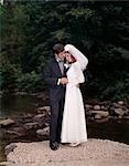 FULL LENGTH PORTRAIT OF BRIDE AND GROOM STANDING ON ROCK BY CREEK OUTDOOR
