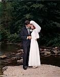 PORTRAIT DE LONGUEUR COMPLÈTE DE LA MARIÉE ET LE MARIÉ DEBOUT SUR ROCK CREEK EN PLEIN AIR