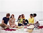 1970s MIXED ETHNIC GROUP TEENAGE COUPLES PICNIC ON BEACH