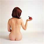 1960s 1970s BACK OF NUDE WOMAN SITTING HOLDING RED APPLE