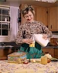 1960s SMILING WOMAN HOUSEWIFE MOTHER WEARING APRON IN KITCHEN POURING MILK INTO THERMOS FOR SCHOOL LUNCH