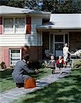 1950s FAMILY WOMAN MOTHER WATCHING MAN FATHER COMING HOME TO SUBURBAN HOUSE KNEELING ARMS EXTENDED TO BOY SON GIRL DAUGHTER RUNNING TO WELCOME HIM HOME