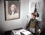 1940s 1950s BOY STANDING BY DESK SPREAD WITH HOMEWORK LOOKING UP AT PAINTING OF GEORGE WASHINGTON