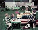 1950s AMERICANA GIRLS AND BOYS IN BUSINESS WITH A LEMONADE AND SNACK FOOD STAND ON THE 4TH OF JULY