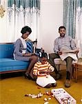 1960s AFRICAN AMERICAN FAMILY MOTHER FATHER SITTING READING LIVING ROOM GIRL DAUGHTER PLAYING FLOOR WITH LEGO TOYS