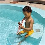 1970s AFRICAN AMERICAN BOY PLAYING WITH TOY BOAT IN BACKYARD SWIMMING POOL
