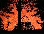1970s COMPOSITE IMAGE SILHOUETTED CHILDREN PLAYING ON SWING SET BY LARGE TREE AT SUNSET