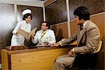 1970s MAN PATIENT MEETING IN DOCTORS OFFICE NURSE WOMAN SHOWING FOLDER TO MALE DOCTOR