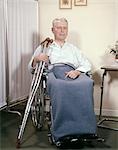 1970s MAN IN WHEELCHAIR HOLDING CRUTCHES IN HOSPITAL