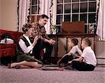 1960s FAMILY WITH TWO SONS GATHERED AROUND RECORD PLAYER LISTENING TO MUSIC INDOOR LIVING ROOM MAN WOMAN BOY